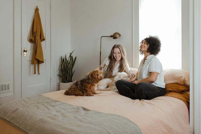 Two people sitting on a bed with a white dog in between them and a smaller orange dog in front of them.jpg